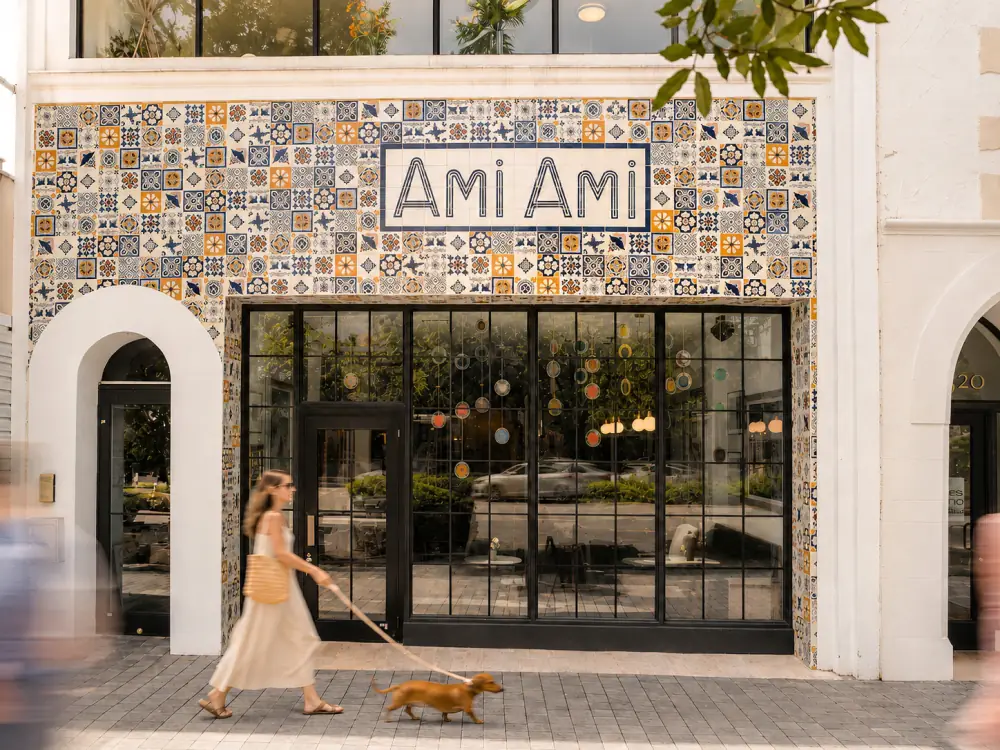Exterior of the Ami Ami café, its storefront window filled with a grid of framed artwork available for purchase